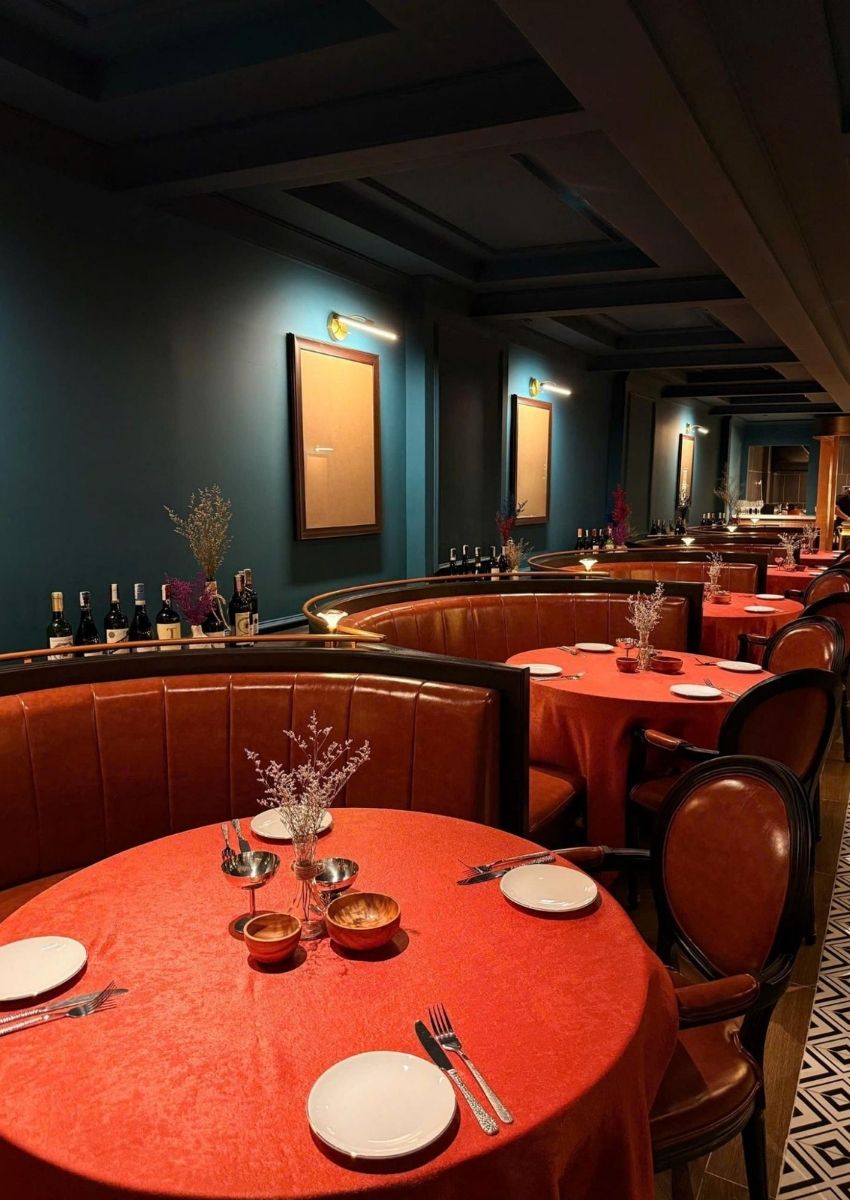 Close-up of a round booth at El Toro, featuring a red velvet tablecloth, minimalist decor, and wine bottles.