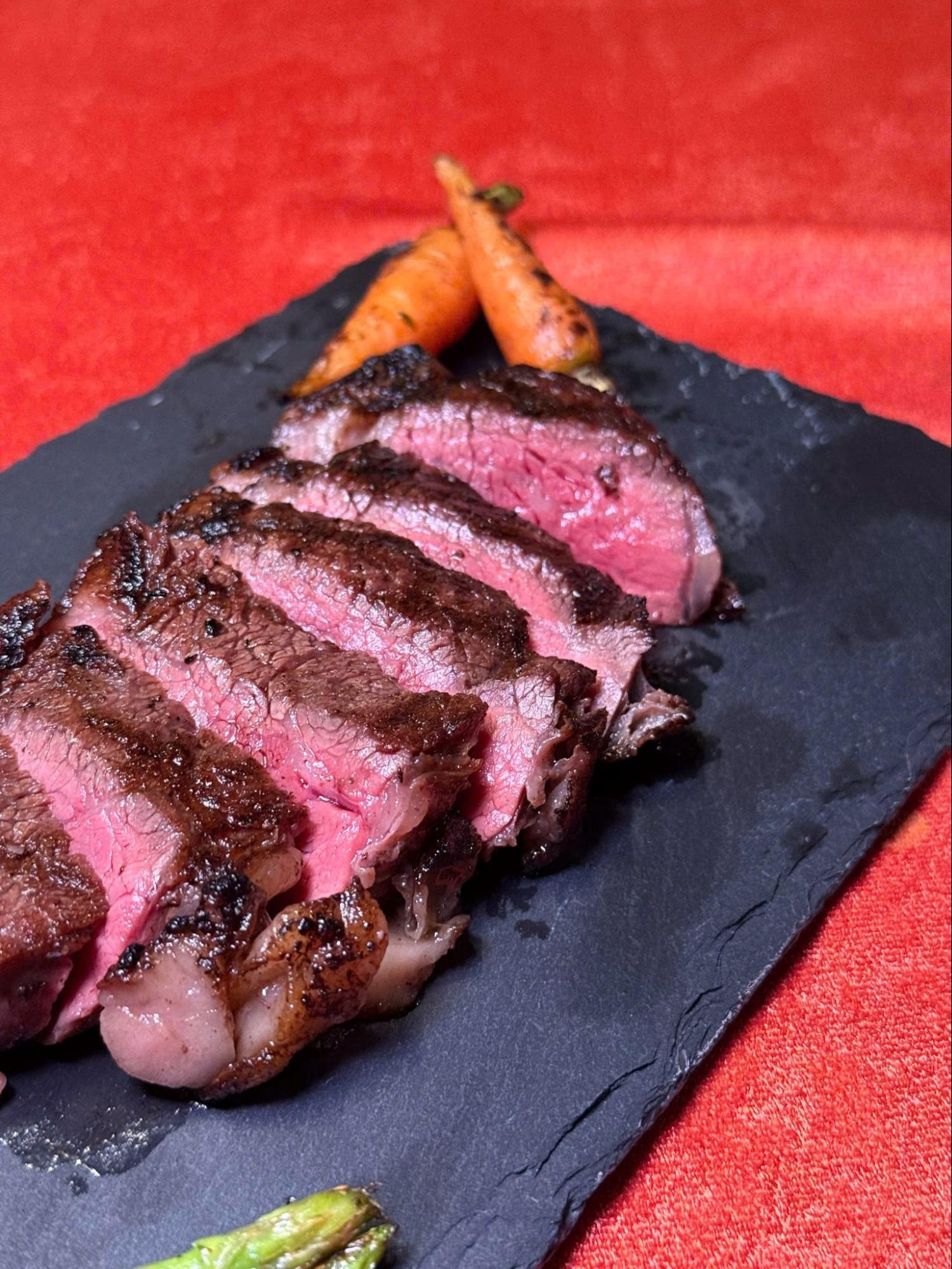 Sous-vide, and smoked steak slices served with grilled baby carrots and asparagus on a slate plate.