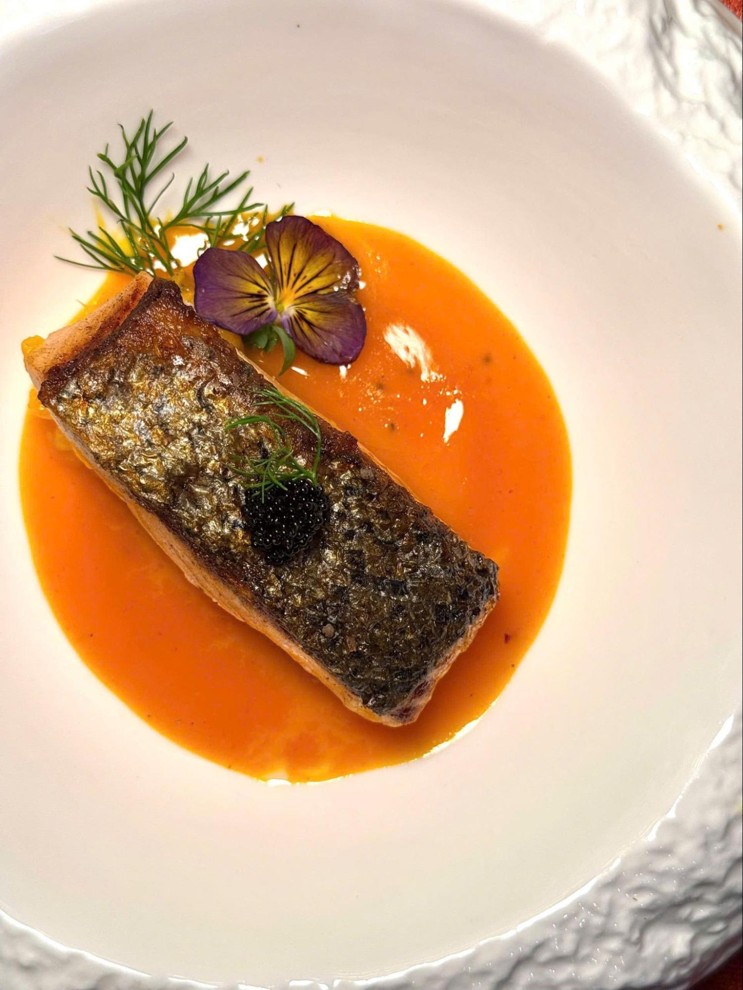 Crispy-skin salmon with caviar, served in fragrant sauce and garnished with dill and edible flowers.