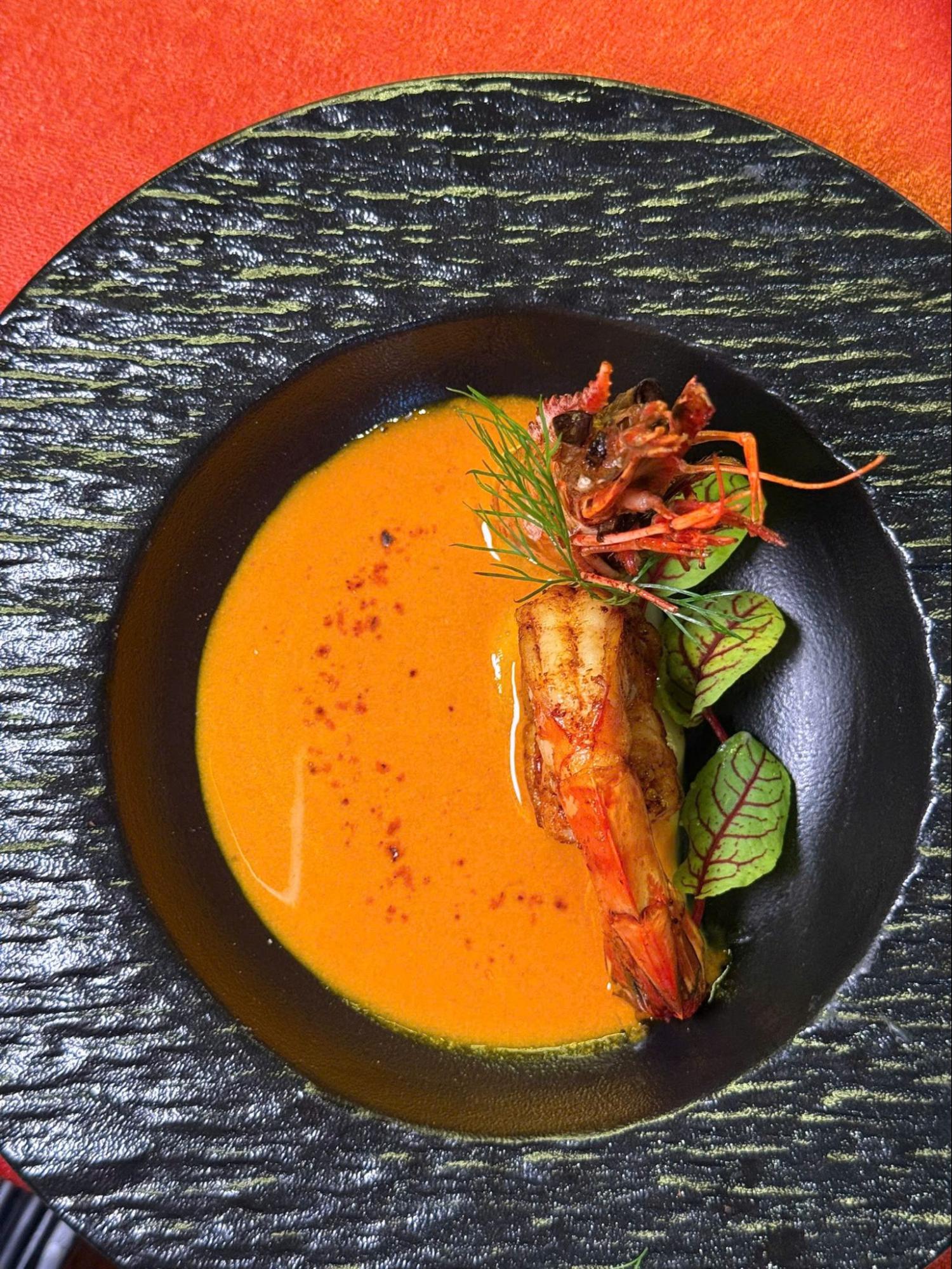 Pumpkin and sweet potato soup with grilled prawn, fresh herbs, and paprika.